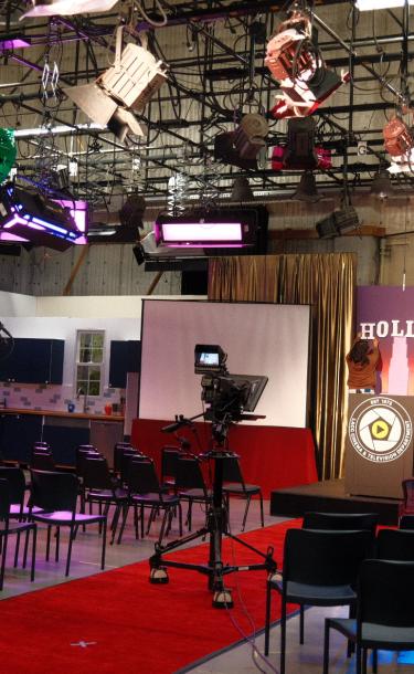 A student hangs up an H on a backdrop of the Hollywood sign for a student Awards Show production in Studio A for a Television Production class