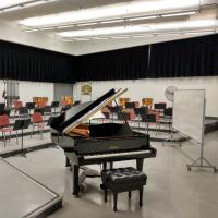 Piano, chairs, stands, and percussion equipment in a large rehearsal room