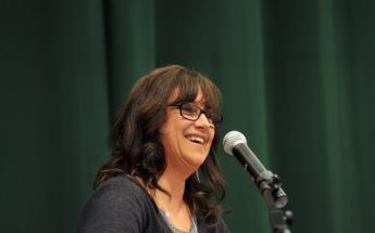 LACC Producer Alumni, Sharon Oreck, speaking at a podium with a dark green curtain backdrop