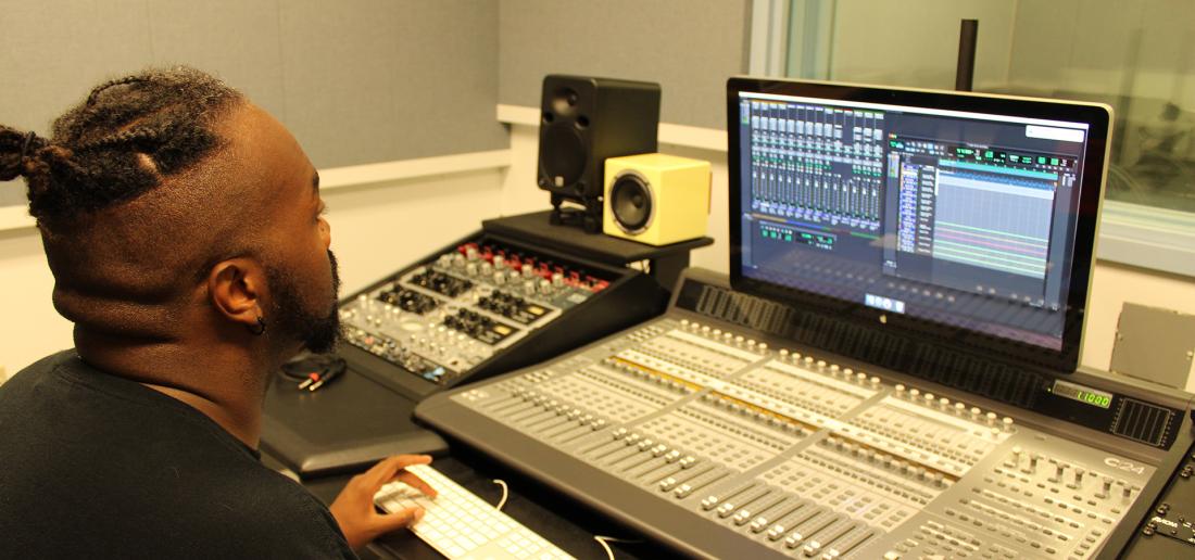 A student works in front of a mixing console and computer running Pro Tools software.