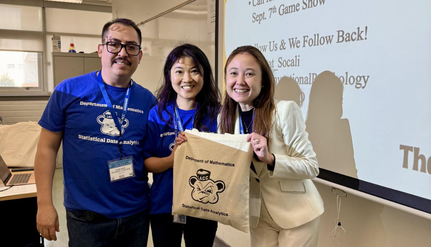 Three faculty members pose with Statistical Data Analytics tote bag